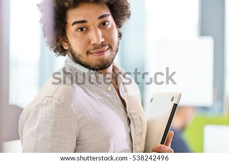 Portrait of confident young businessman holding laptop at office