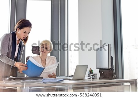 Businesswoman and female manager reading book at desk in office