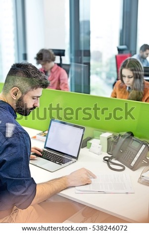 Businessman reading book while using laptop in office