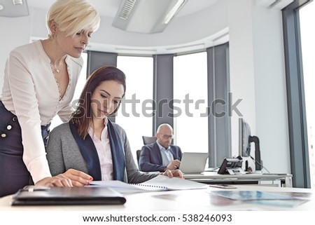 Businesswomen reading project with male colleague in background at office