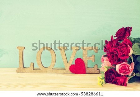 Valentines day background. Word LOVE from wooden letters and red heart next to beautiful bouquet of roses on old table. Filtered image