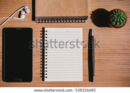top view of work desk with open notebook, pen, smartphone, earphones and cactus - hard shadow 