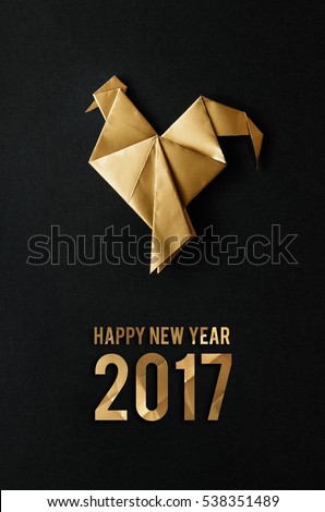 Golden shiny paper folded rooster handmade origami craft on black background. Nice natural vertical holiday greeting card. Happy new year 2017 text lettering.
