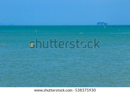 Beautiful yellow and orange buoys are floating in blue sea on sunny day with islands and blue sky background