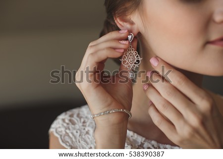 Wedding earrings on a female hand, she takes the earrings, the bride fees, morning bride, white dress, wear earrings Royalty-Free Stock Photo #538390387