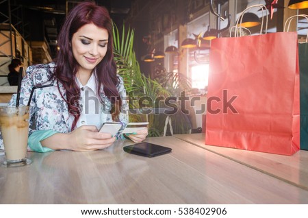 Girl sits at the table and buys over the Internet with their mobile and credit card, Business woman resting after buying and check balance on her bank account. The girl spent a lot of money