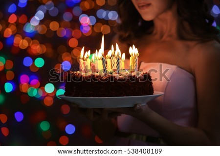 Young woman holding plate with tasty birthday cake against defocused lights