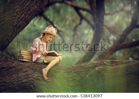 A pretty little blonde girl in a straw hat reading a book on a large spreading tree. Children and science. Royalty-Free Stock Photo #538413097