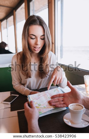 Vertical image of Man and girl sitting by the table with map in cafe near the sea on date. First-person view