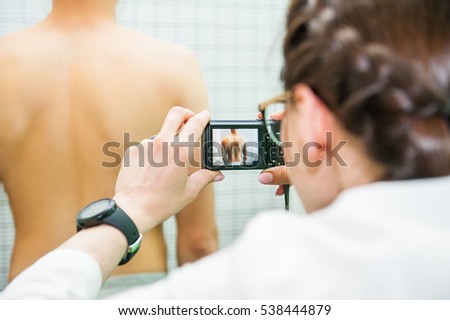 Close up Female Physiotherapist in her practice, makes photo shoot of the male pacient's back