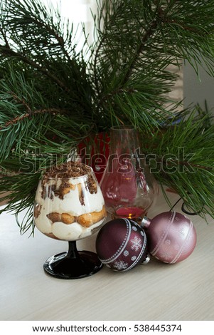 Traditional Italiano tiramisu dessert in a glass goblet with a burning candle on the background of the Christmas tree. Selective focus.