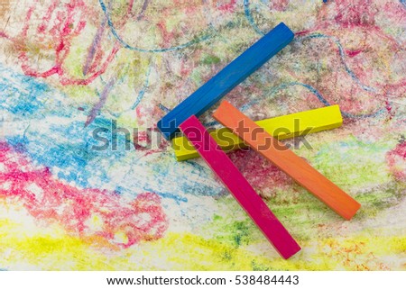 View of a group of differently colored chalk lying on colorful drawings of paper