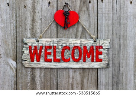Red welcome sign with  country wooden heart with black iron house keys hanging by rope on antique rustic wood door; Valentine's Day background