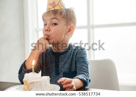 Image of birthday boy sitting in kitchen near cake and eating. Look at camera.
