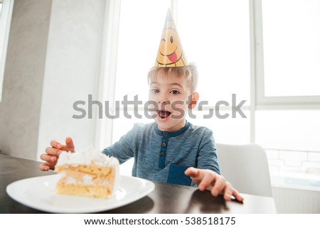 Image of happy birthday boy sitting in kitchen near cake and eating. Look at camera.