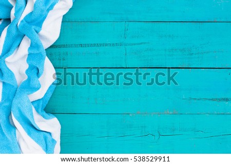 Blank rustic teal blue wood beach sign with turquoise and white striped beach towel border; blue painted background with copy space 