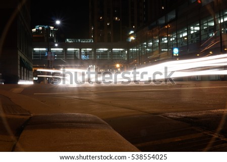 Light trails at night through downtown Minneapolis Minnesota. Brake and headlights streak glows down busy city street circle lens flare viniette on camera