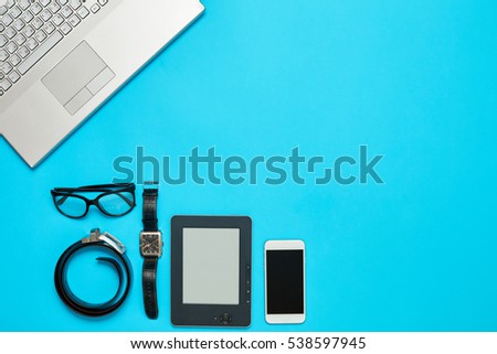 Image of blue Office Desk with laptop Keyboard, phone, watch, ebook, glasses, and belt. Supplies Top View. Business and workplace concept