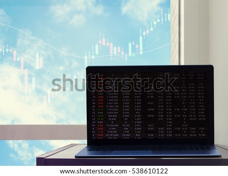 computer on table near glass window with stock chart on screen on blue sky background : nature and business concept