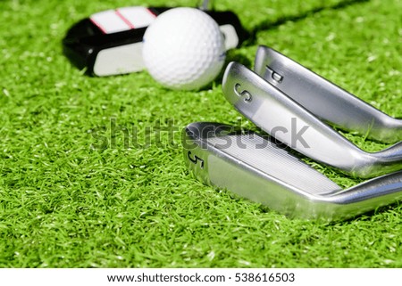 Golf ball and golf club on green grass background.