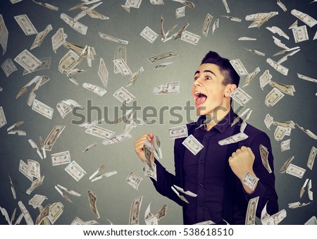 Portrait happy man exults pumping fists ecstatic celebrates success under money rain falling down dollar banknotes isolated on gray wall background