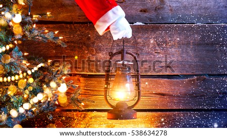 Santa Claus hand holding vintage oil lamp over Christmas holiday wooden rural background. Beautiful Empty Christmas room. New Year Background. Search, searching concept