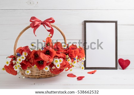 Card for Valentine Day. Red poppies bouquet in basket with bow and motivational frame with heart and place for your text or picture on background of white wooden planks in scandinavian style 