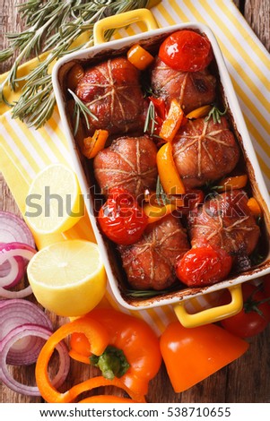 Ballotine rabbit baked with tomatoes, pepper and rosemary close up in baking dish on the table. vertical view from above

