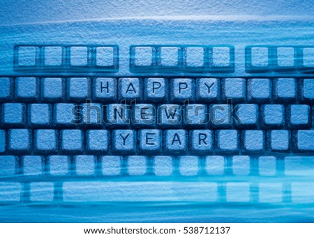 keyboard covered with snow with words Happy New Year illuminated with blue light