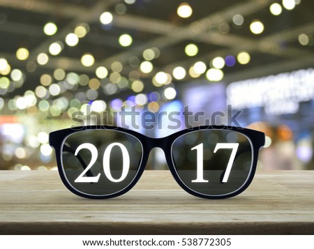 2017 text with eye glasses on wooden table over blur light and shadow of shopping mall, Business vision concept