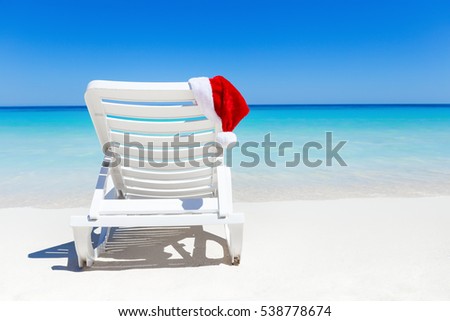 Santa Claus Hat on sunbed near tropical calm beach with turquoise caribbean sea water and white sand. Christmas vacation celebration Royalty-Free Stock Photo #538778674
