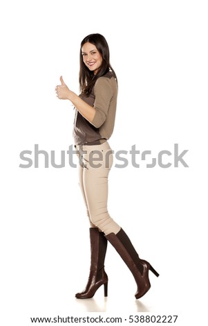 side view of young woman in trousers and high boots posing on white background