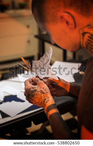 Male tattooer cutting with scissors paper sketch for tattoo, preparing for tattooing