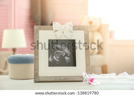 Frame with ultrasound photo and pacifier on table