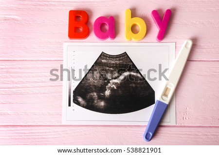 Ultrasound photo and pregnancy test on wooden background