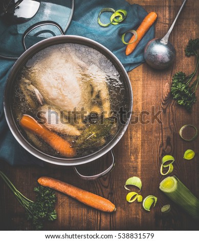 Chicken soup cooking, pot with chicken broth and  ladle on dark rustic wooden background with vegetables ingredients, top view. Healthy food or Diet nutrition concept