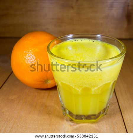 Orange and freshly made orange juice in transparent glass on walnut wood surface.