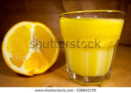 Half of orange and freshly made orange juice in transparent glass on wooden kitchen table.