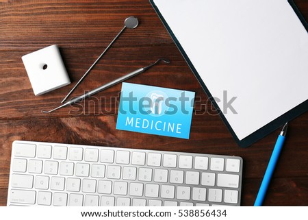 Business card, clipboard, keyboard and dental tools on wooden background