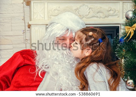 Santa Claus with a little girl sitting near the fireplace.