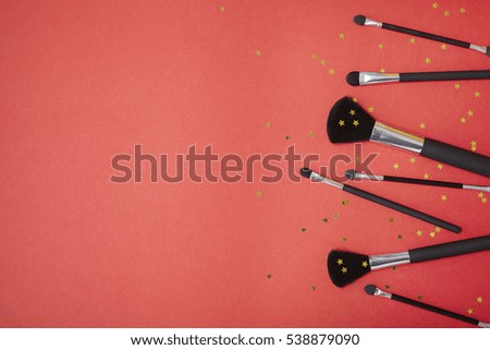 Cosmetic make up brushes on a bright red background with gold glitter stars