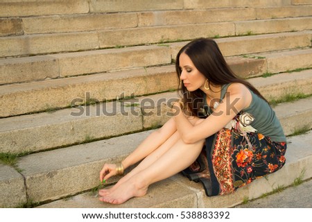 Pensive girl in a long skirt sitting on the stairs. Warm colors.