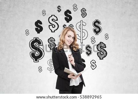 Portrait of a redhead businesswoman standing with a notebook and a pen near a concrete wall with dollar signs drawn on it. Concept of making money