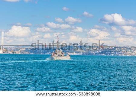 Naval vessel passing though Bosphorus  Bridge with background of Bosphorus strait on a sunny day with background cloudy blue sky and blue sea in Istanbul, Turkey. Blue Turkey concept.