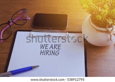 WE ARE HIRING word written on paper with glass, smartphone and green plant, copyspace area
