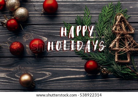 happy holidays text sign on christmas tree and red and golden ornaments on rustic wooden background with space for text. flat lay. seasonal greetings concept. winter holidays.