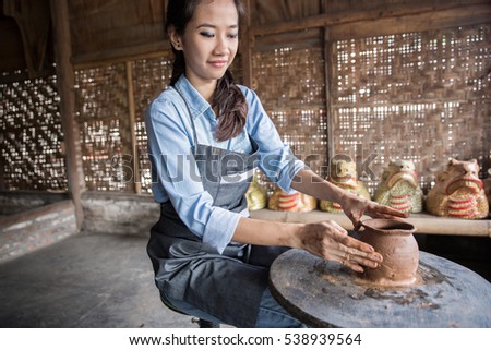 asian woman making vase from fresh wet clay on pottery wheel