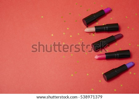 Assorted color lip stick make up on a bright red background with gold glittery stars and empty space at side