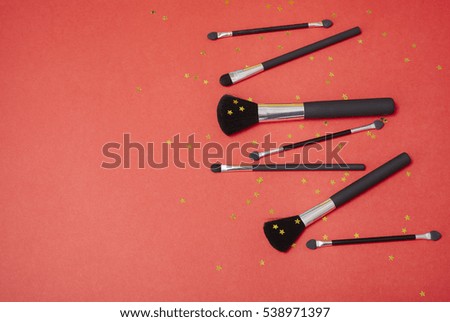 Cosmetic make up brushes on a bright red background with gold glitter stars and blank space at side