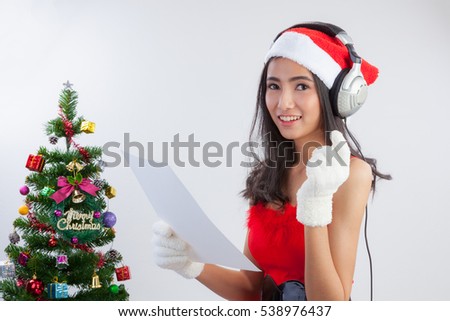 Beautiful girl wearing a Santa hat listening to music and singing Christmas carols. in Santa Claus costume at home. Christmas time.